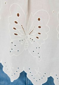 Tessuto bianco ricamato con un design di farfalla caratterizzato da dettagli a taglio, bordi ondulati e sottili accenti blu vicino all'orlo.