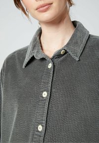 Szara koszula z kordurowego materiału o teksturowanej powierzchni, z zapięciem na guziki i miękkim, prążkowanym kołnierzykiem. Posiada jasne guziki i luźny krój.