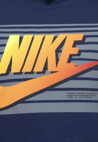 Marineblaue kurzärmelige Hemd mit auffälligem orangefarbenem und grauem "NIKE"-Logo sowie Swoosh-Design auf einem gestreiften Hintergrund mit strukturiertem Druck.
