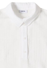 Chemise blanche à col avec trois boutons et un motif rayé vertical texturé, avec une étiquette cousue à l'arrière du col.
