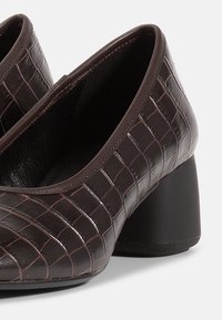 Pantofi din piele maro cu textură de crocodil, vârf rotund și toc mediu de tip bloc. Cusături vizibile pe margini.