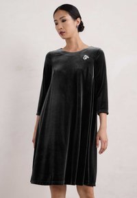 Schwarzes Samtkleid mit drei Viertelärmeln, A-Linie, runden Halsausschnitt und floralem Broschen-Detailing auf der oberen linken Seite.