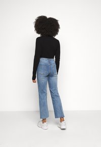 Jeans blu a vita alta con taglio dritto, orlo grezzo e due tasche posteriori, abbinati a un top fitted nero a maniche lunghe.