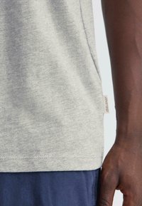 Világosszürke t-shirt sima textúrával, oldalsó varrással és egy kis címkével az alján, sötétkék sorttal párosítva.