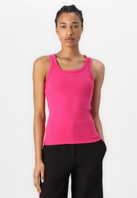 Enganliegendes ärmelloses Tanktop aus leuchtend pinker Baumwolle, mit rundem Ausschnitt und dezentem "HUGO"-Logo in der Mitte. Glatte Textur, minimales Design.