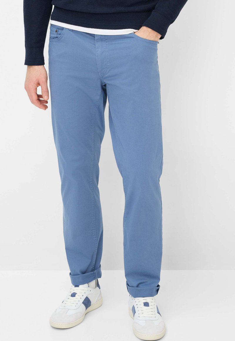 Hellblaue Baumwoll-Chinos mit geradem Bein, leicht elastisch, umgeschlagenen Bündchen und Seitentaschen. Kombiniert mit weißen Sneakern.