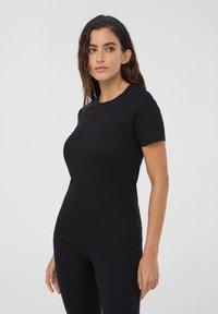 Czarny t-shirt z krótkim rękawem, wykonany z gładkiego materiału, z okrągłym dekoltem, dopasowanym fasonem i bez widocznych wzorów ani elementów metalowych.