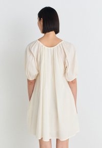 Kokvilnas kleita off-white krāsā, ar īsām pūkām, apaļu kakla izgriezumu un brīvu augšdaļu ar savilktām detaļām aizmugurē.