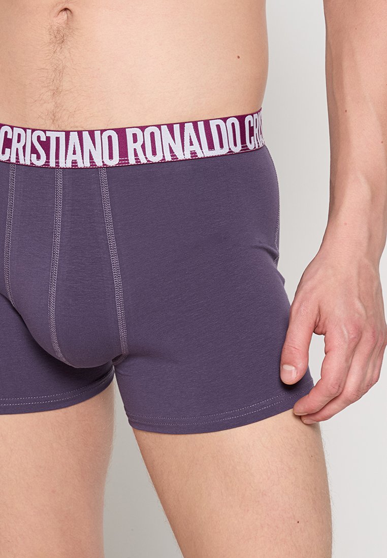 Calzoncillos boxers para hombre en color morado con una cinturilla elástica blanca de marca que presenta "CRISTIANO RONALDO" en letras gruesas. Textura suave y diseño ajustado.