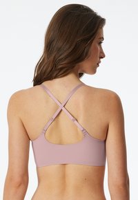 Light pink sports bra with a crisscrossed strap design, featuring a scoop back and smooth fabric texture. Adjustable strap hardware detailed.