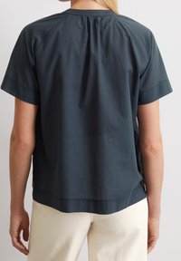 Kortärmad topp i mörkblått tyg med lös passform, rund halsringning, veckdetalj i ryggen och en lätt böjd nederkant.