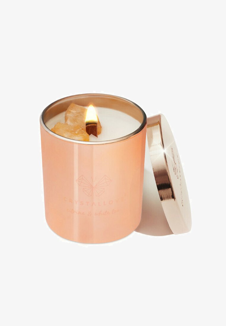 Bougie en or rose dans un récipient en métal rond avec une mèche en bois, allumée, mettant en valeur une cire blanche et un petit accent en cristal sur le dessus.