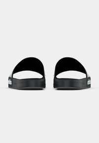 Μαύρες πέδιλες με ανοιχτή πίσω σχεδίαση, υφασμάτινη σόλα και λευκή επωνυμία στη λωρίδα. Καθαρός, μινιμαλιστικός προφίλ με ομαλή επιφάνεια.