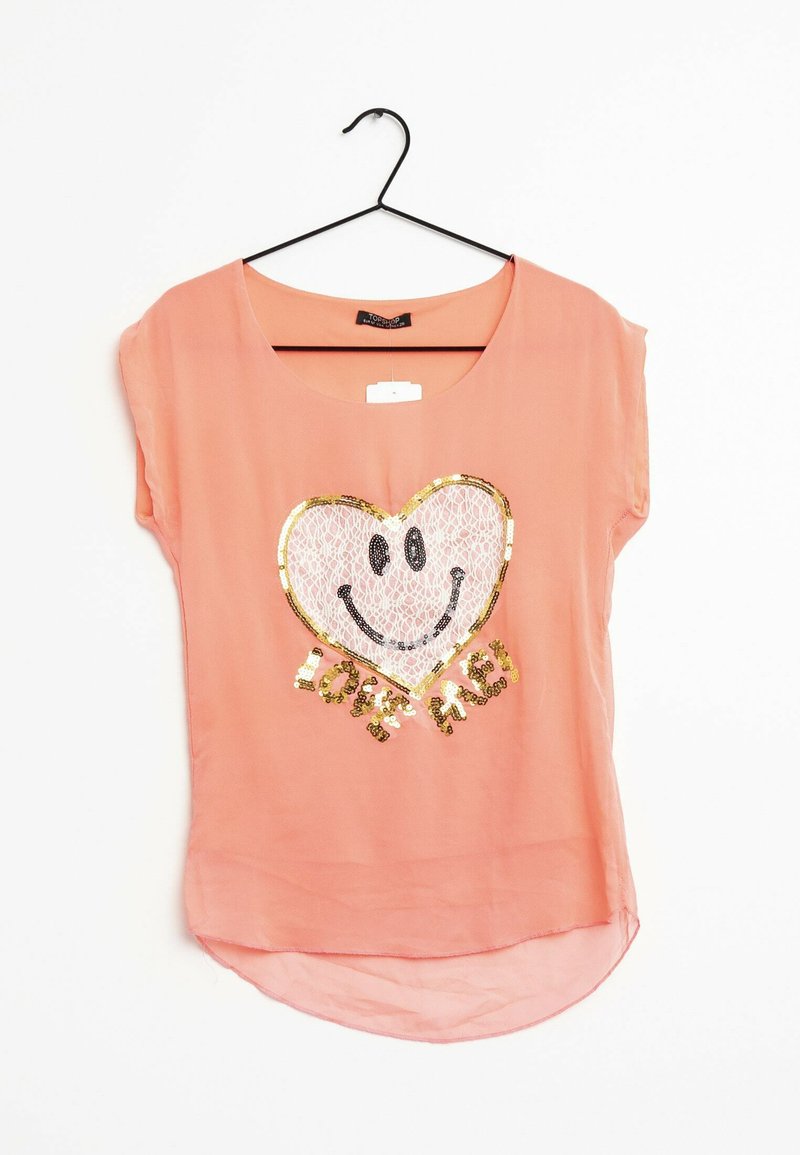 Haut pêche à manches courtes, col rond, présentant un cœur en sequins avec un visage souriant et le texte "LOVE ME" en doré et noir.