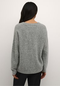 Suéter gris de punto suave y texturizado con escote redondeado y mangas largas. Corte ligeramente holgado, que muestra una silueta relajada.