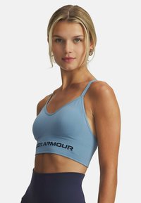 Šviesiai mėlynas sportinis liemenėlis su grioveliniu paviršiumi, su žemu apykakle ir „Under Armour“ logotipu per apatinį dirželį. Reguliuojamos petnešėlės.