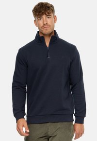 Marineblå quarter-zip pullover lavet af blødt stof. Har lange ærmer og ribbestrikkede manchetter. Subtilt logo nær kraven tilføjer detalje.