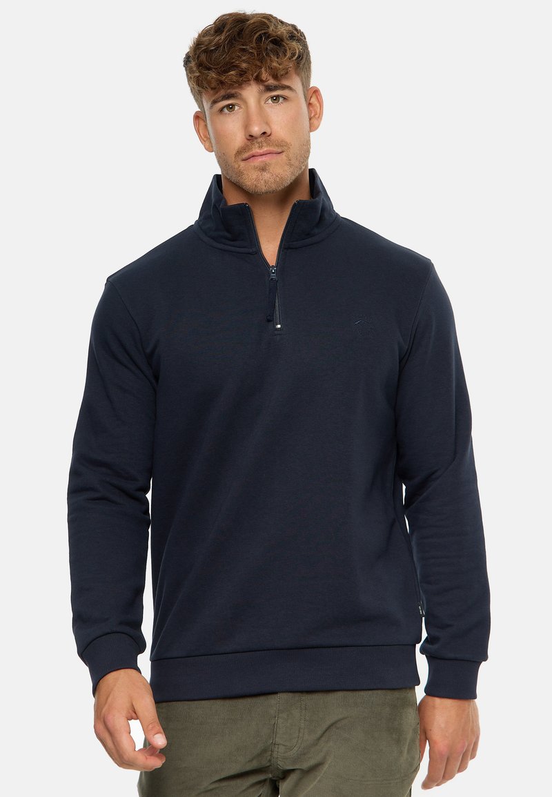 Marineblå quarter-zip pullover lavet af blødt stof. Har lange ærmer og ribbestrikkede manchetter. Subtilt logo nær kraven tilføjer detalje.