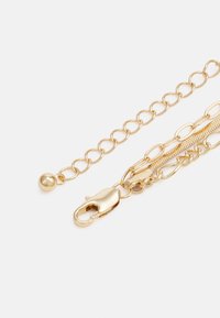 Corrente de ouro com elos entrelaçados e fecho de clipe. Possui um detalhe em forma de esfera lisa e uma seção texturizada, refletindo a luz.