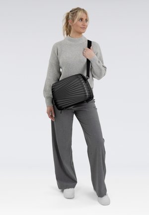 Borsa a tracolla nera con una forma rettangolare, texture liscia e tracolla regolabile, indossata sopra un maglione grigio e pantaloni grigi.