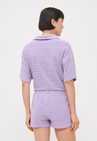 Lila- och vitrandig kortärmad polo med matchande shorts, med mjuk textur och avslappnad passform. Bakvy visas.