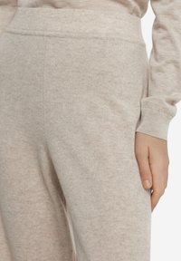 Beige loungebyxor i bomullsblandning med en mjuk, texturerad yta, utrustade med resårmidja och åtsittande manschetter. Minimalistisk design.