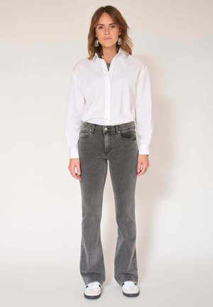 Chemise blanche boutonnée, jeans évasés gris et baskets blanches. Tissu lisse, lignes épurées et détails de couture subtils sur le pantalon.