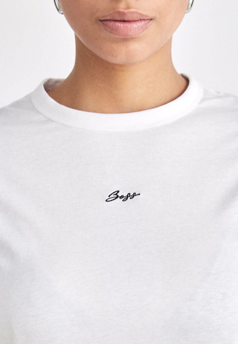 T-shirt en coton blanc avec un col rond et des manches courtes, orné de texte brodé noir sur la poitrine.