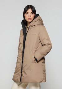 Beige parka med svart huva, dragkedjestängning och sidofickor. Har "POLO CLUB"-logotyp på bröstet. Slät, vattenavvisande material.