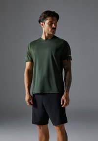 Dark green athletic t-shirt with a smooth texture, short sleeves, and subtle paneling. Paired with black shorts, featuring a simple design.