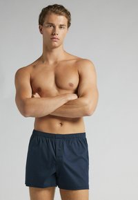 Granatowe kąpielówki z elastycznym paskiem i zapięciem na guzik, wykonane z lekkiego materiału, z bocznymi kieszeniami i luźnym krojem.