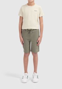 Beige katoenen t-shirt met "BALLIN" logo, olijfgroene shorts met een trekkoord en zijzakken, gecombineerd met witte sneakers met groene strepen.