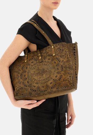 Borsa tote in pelle marrone con intagli floreali intricati e incisioni in rilievo, dotata di due robuste spalline e dettagli decorativi in metallo.