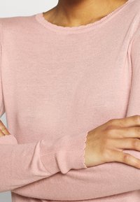 Rosa stickad tröja med ribbat rundhals och vågiga manschetter, med en mjuk textur och nära passform.