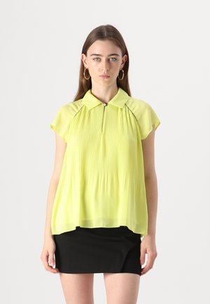 Heldere gele blouse met een geplooid ontwerp, korte mouwen en een kraag. Draag het over een zwarte rok, gemaakt van lichte, soepele stof.