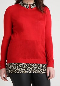 Pull rouge à manches longues avec un col imprimé léopard, superposé à un haut beige à motif léopard, présentant une coupe droite et une texture douce.