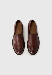 Brown leather loafers featuring a rounded toe, recessed stitch detailing, and a slight heel, with a contrasting black rubber sole.