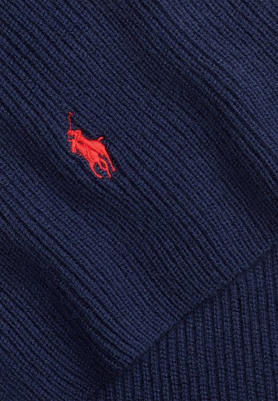 Zbliżenie granatowego prążkowanego dzianego materiału z czerwonym, haftowanym logo polo gracza.