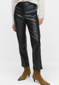Zwarte neplederen broek met een slank model en een rechte pijp. Kenmerkt zich door een soepele textuur en een hoge taille. Gecombineerd met bruine puntige laarzen.