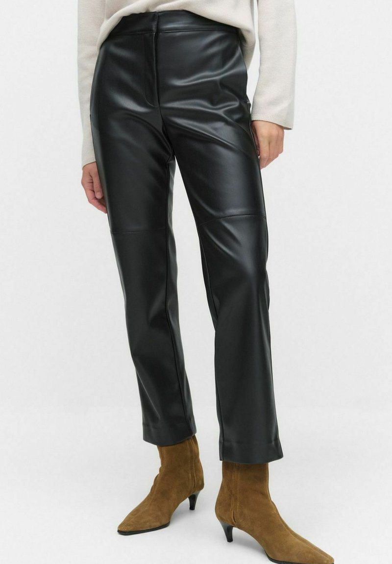 Zwarte neplederen broek met een slank model en een rechte pijp. Kenmerkt zich door een soepele textuur en een hoge taille. Gecombineerd met bruine puntige laarzen.