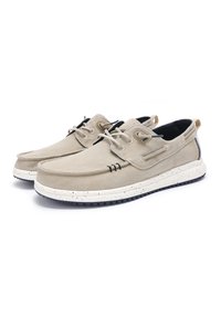 Beige canvas shoes with a white speckled rubber sole, lace-up design, and navy accents. Features side grommets and stitched detailing.