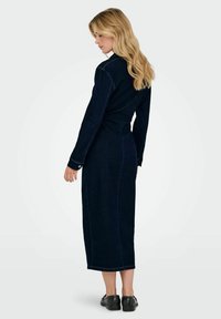 Robe chemise en denim foncé avec des manches longues, des poignets à boutons et une taille cintrée, présentant des coutures visibles et un ourlet droit arrivant aux chevilles.