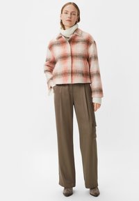 Kraciasta kurtka w odcieniach różu i brązu o skróconym kroju, zestawiona z oliwkowymi spodniami o wysokim stanie i białym golfem.