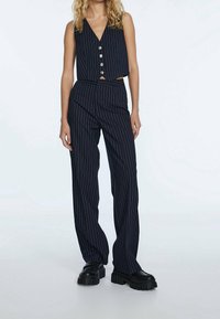 Conjunto a rayas en azul marino que incluye un top corto sin mangas con escote en v y botones, y pantalones de pierna ancha de cintura alta. Tejido texturizado y zapatos gruesos.