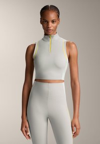 Light gray sports crop top with a high neck, yellow accents on the shoulders, and matching high-waisted leggings. Smooth, stretchy material.