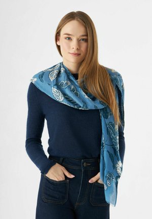 Une écharpe bleue avec des motifs de feuilles et de fleurs blancs, en tissu léger, drapée lâchement autour du cou.