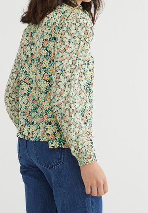 Blusa floreale verde, con un motivo di fiori multicolori, maniche lunghe con polsini arricciati e un collo leggermente arricciato.