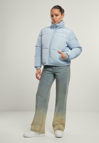 Lyseblå pufferjakke med høj krave og broderet logo. Har sidelommer og ribbede mansjetter. Sammen med slidte wide-leg jeans.