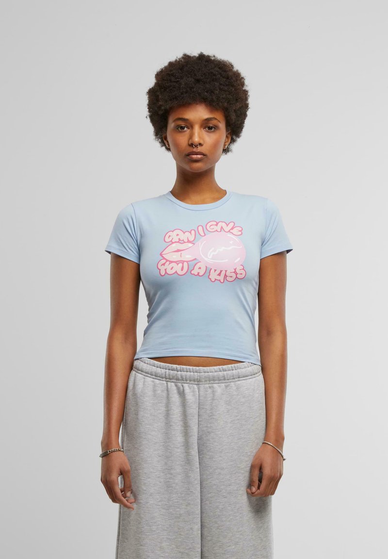Light blue crop top made from soft fabric featuring a graphic in pink text that reads "CAN I GIVE YOU A KISS" alongside pink lips and bubble graphic.