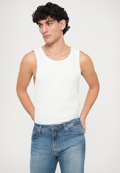 Weißes ärmelloses Tanktop aus geripptem Stoff, kombiniert mit hellblauen Jeans im klassischen Schnitt und mit fünf Taschen.